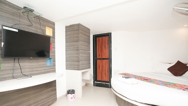 A modern bedroom with a large bed, a flat-screen TV mounted on a wall, and a wooden door. - Hotel Havana (Mumbai)