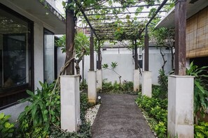 A narrow pathway flanked by white pillars and lush greenery, leading to a modern building with large windows. - Queen Rose Villa & Spa (Jimbaran)