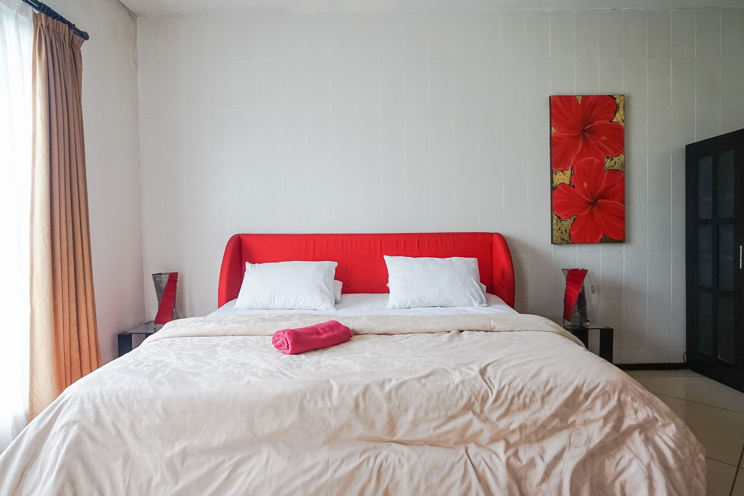 A hotel room with a red headboard, white bedding, and a large floral artwork on the wall.