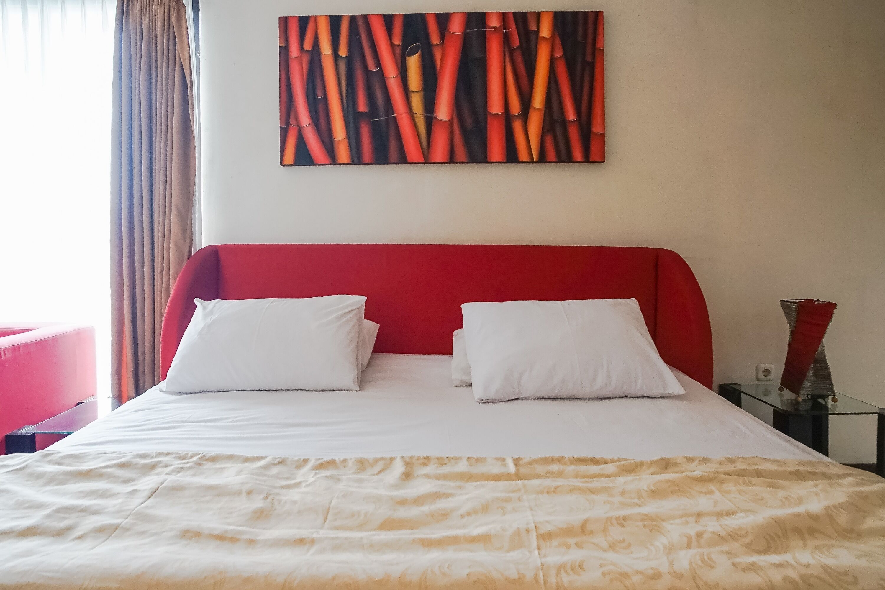 A hotel room with a red headboard, white bedding, and a large abstract painting on the wall.