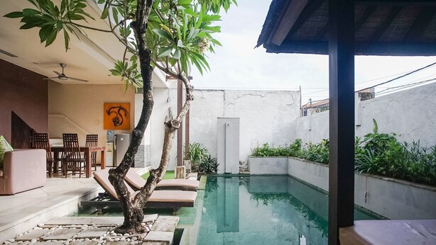 Uma área de piscina com vista clara da piscina, uma árvore e um espaço de refeições com cadeiras e uma mesa.