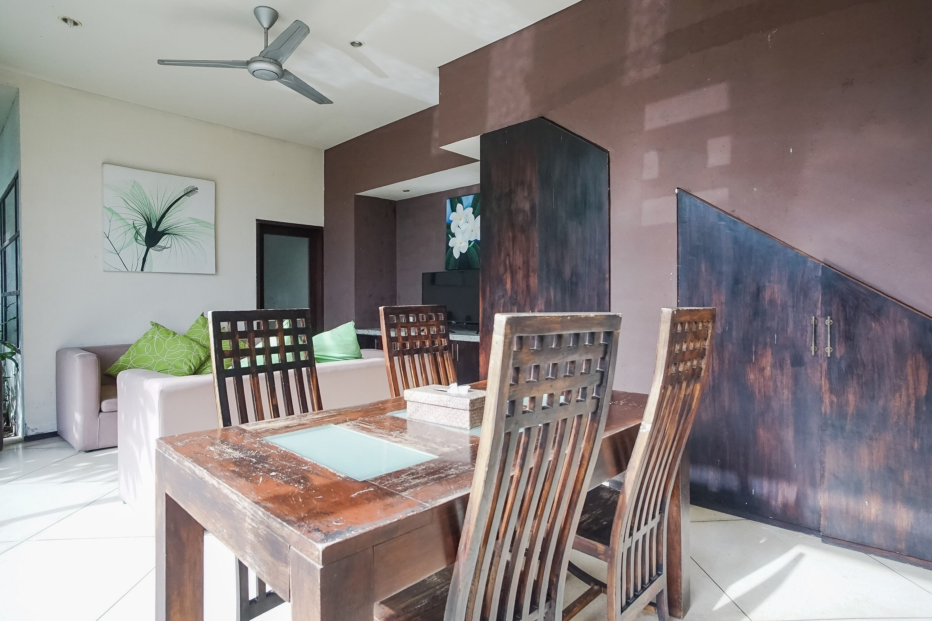 A dining area with a wooden table and chairs, a ceiling fan, and a large painting on the wall.