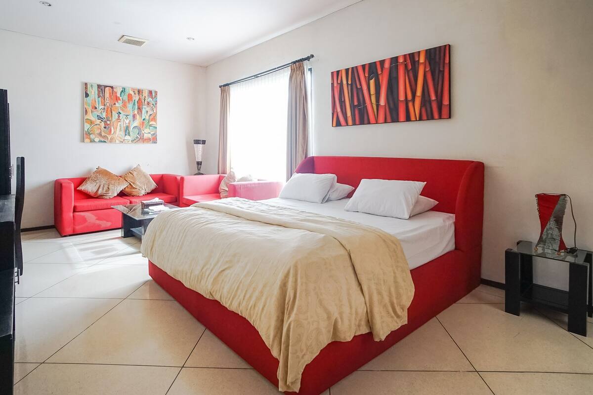 A hotel room with a red bed, a red sofa, and two paintings on the walls.