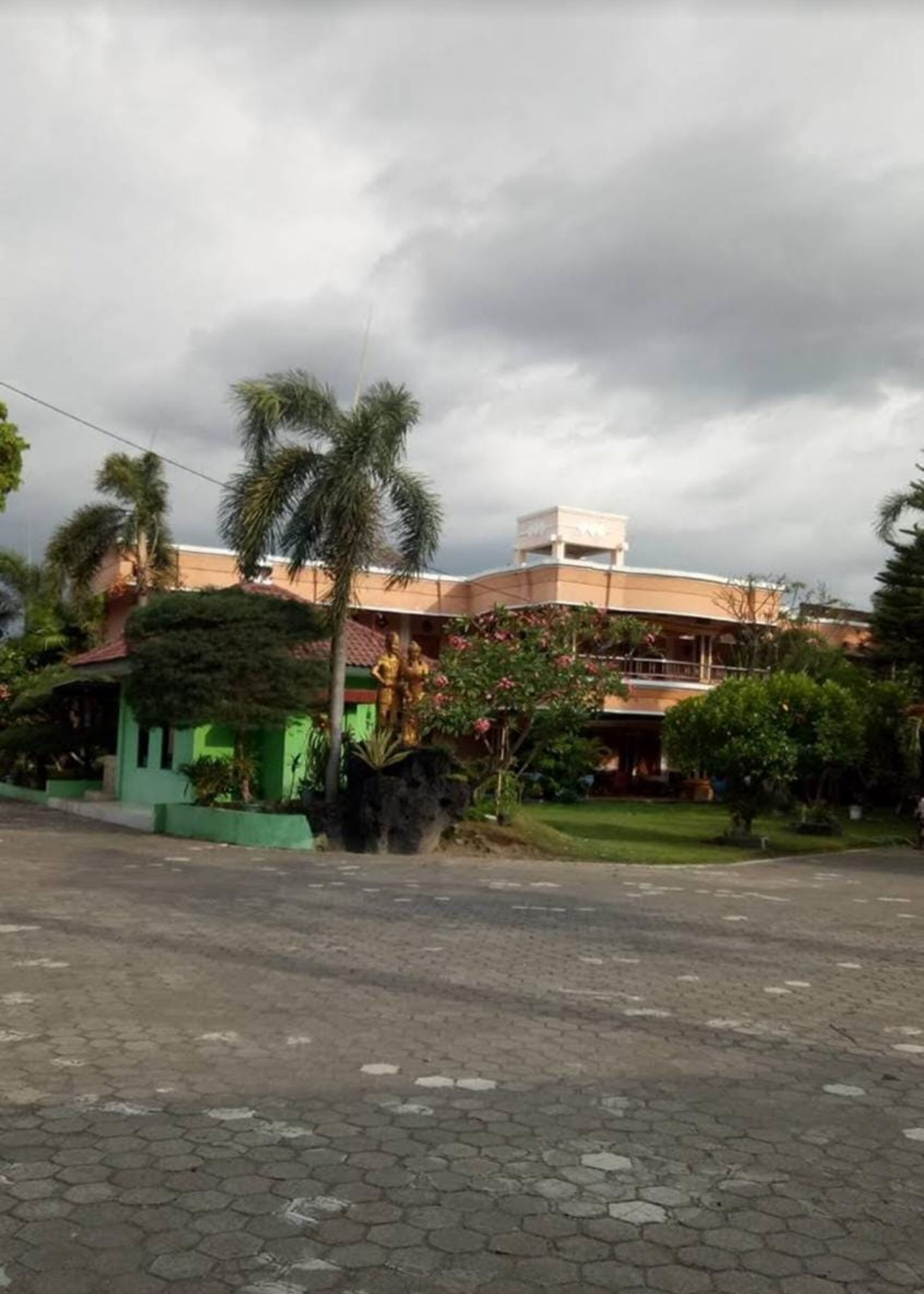 A building with a green facade, a white upper section, and a paved area in front.