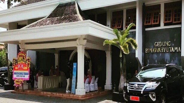 Un bâtiment doté d’une entrée couverte, d’un palmier et d’un SUV noir garé devant.