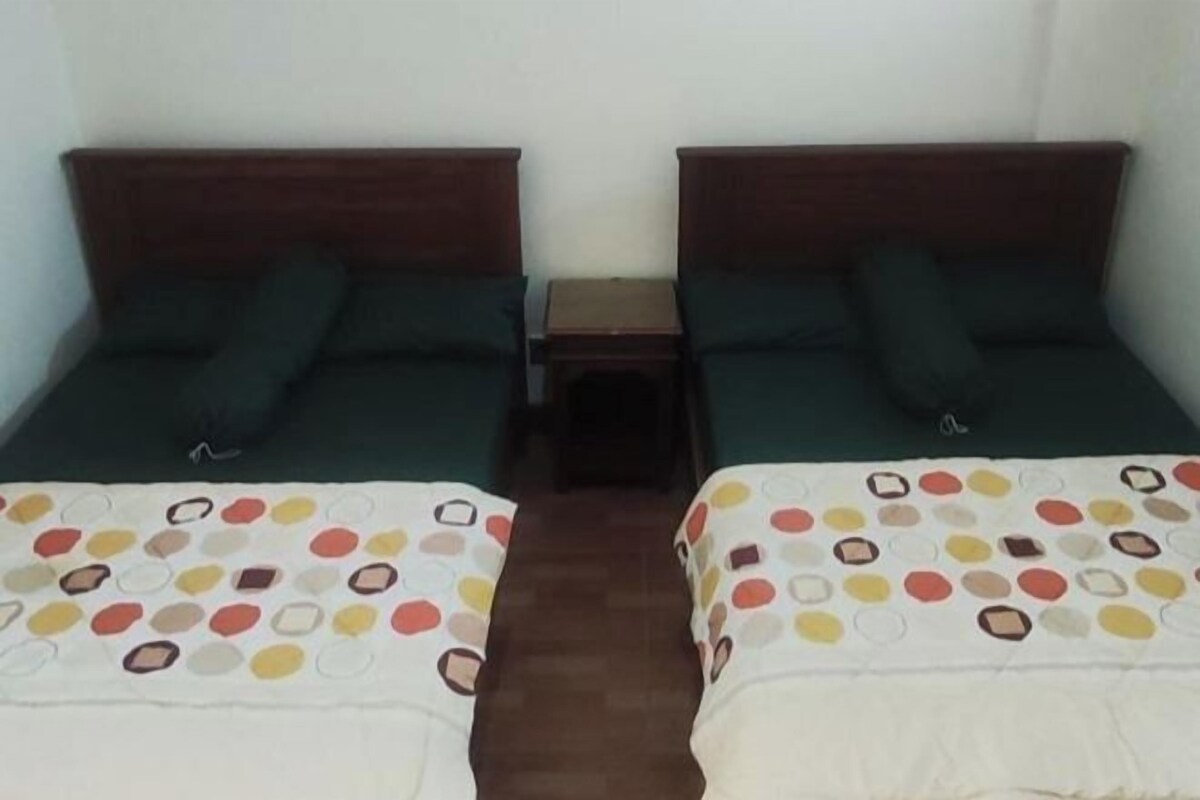 A room with two single beds, each with a wooden headboard, a small bedside table, and a colorful bedspread.