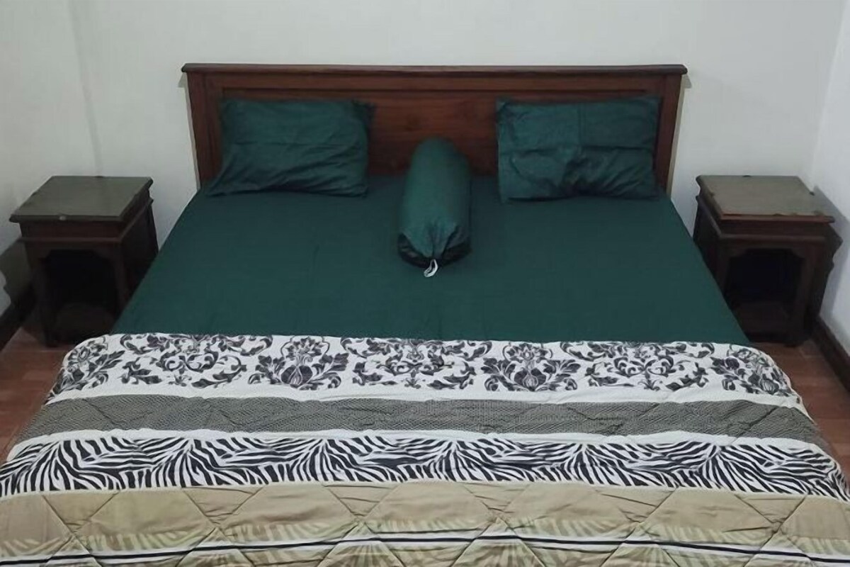 A bed with a green bedspread and multiple pillows, flanked by two nightstands.