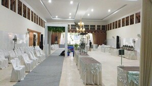 Un vaste hall avec des rangées de chaises et de tables blanches, un lustre et une scène.