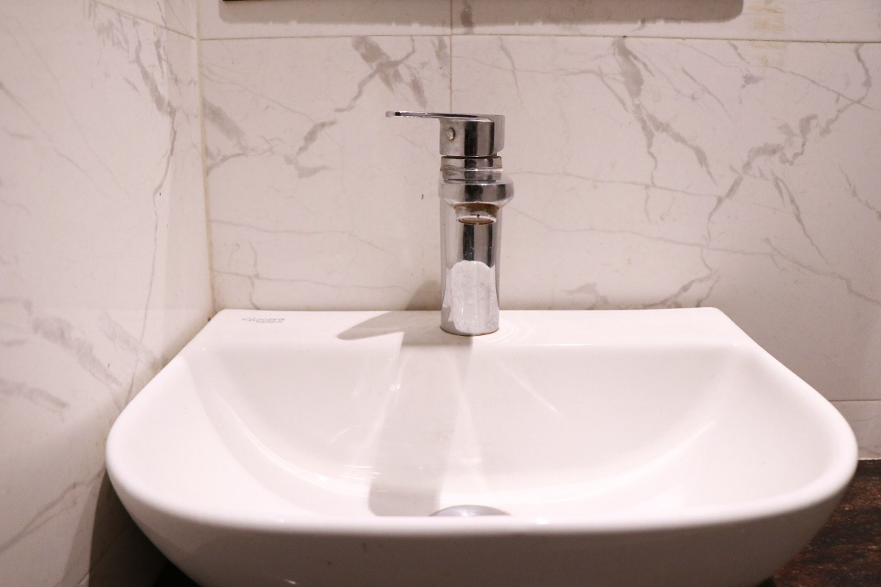 A white bathroom sink with a chrome faucet and marble walls.