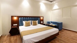 A hotel room with a large bed, a bedside table, a chair, and a wall-mounted TV. - Hotel Amrit Near Old Delhi Railway Station (New Delhi)