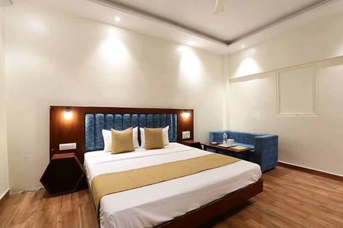 A hotel room with a large bed, a bedside table, a chair, and a wall-mounted TV.