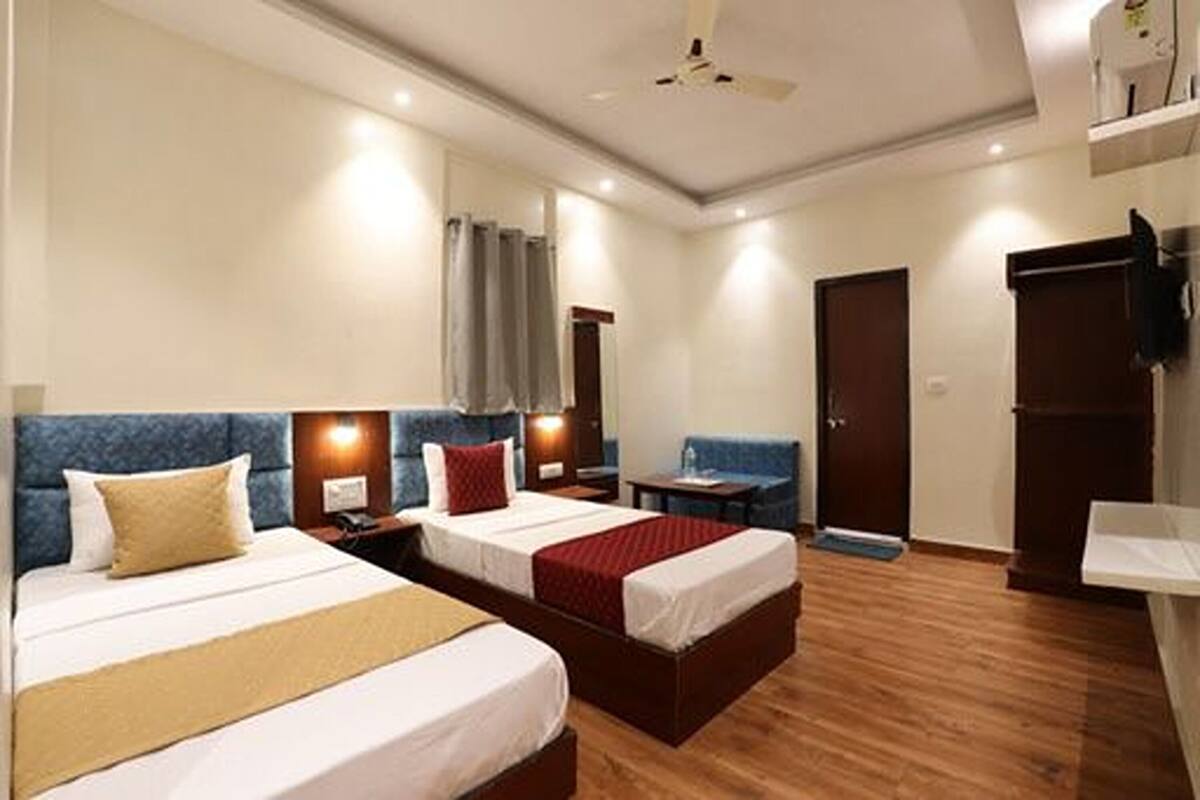 A hotel room with two beds, a desk, a chair, a wardrobe, and a ceiling fan.
