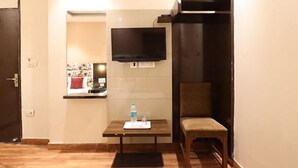 A hotel room with a bed, a TV mounted on the wall, a small table with a water bottle, and a chair. - Hotel Amrit Near Old Delhi Railway Station (New Delhi)