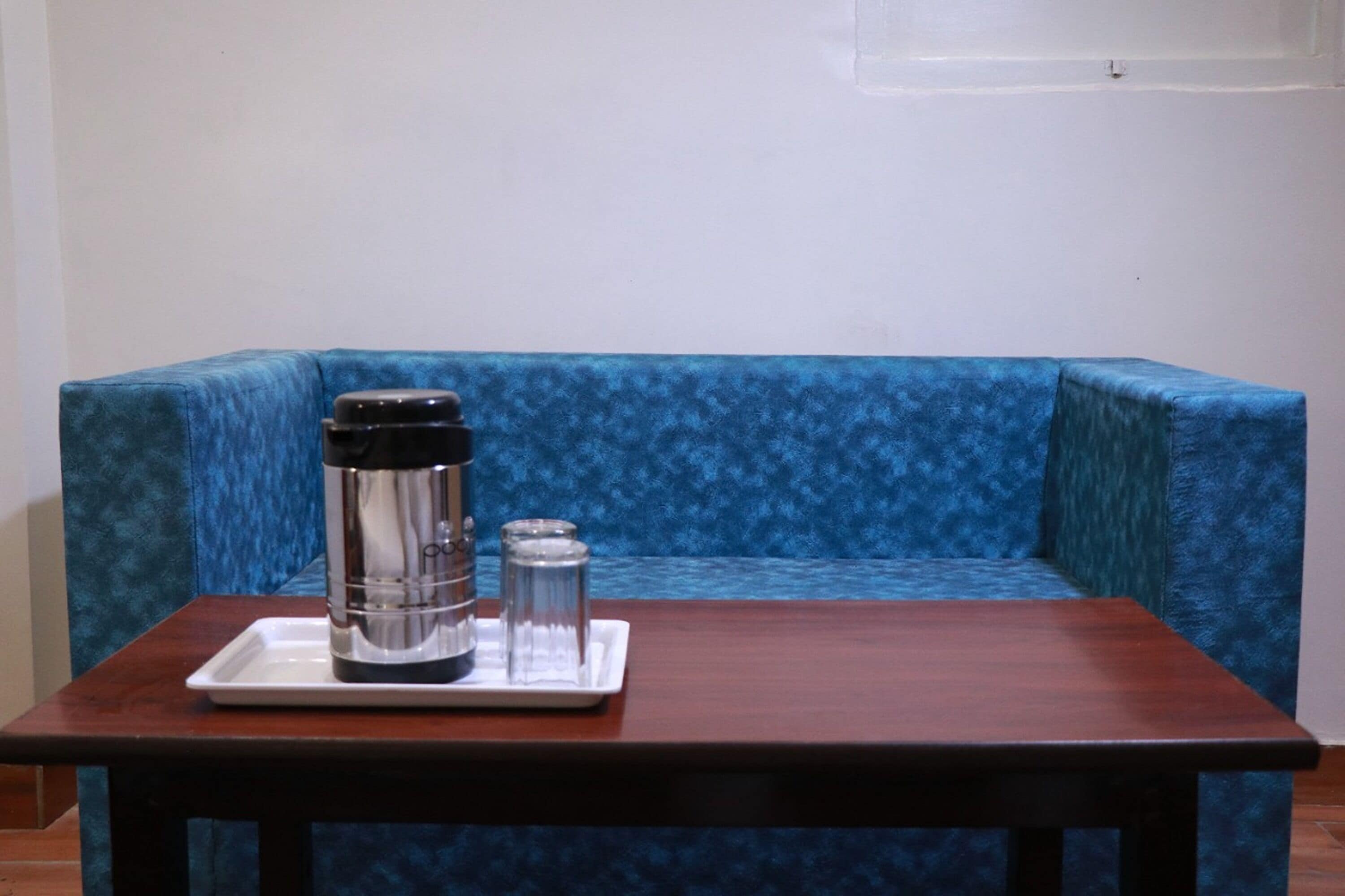 A small table with a coffee maker and a glass on a tray, placed in front of a blue upholstered sofa.