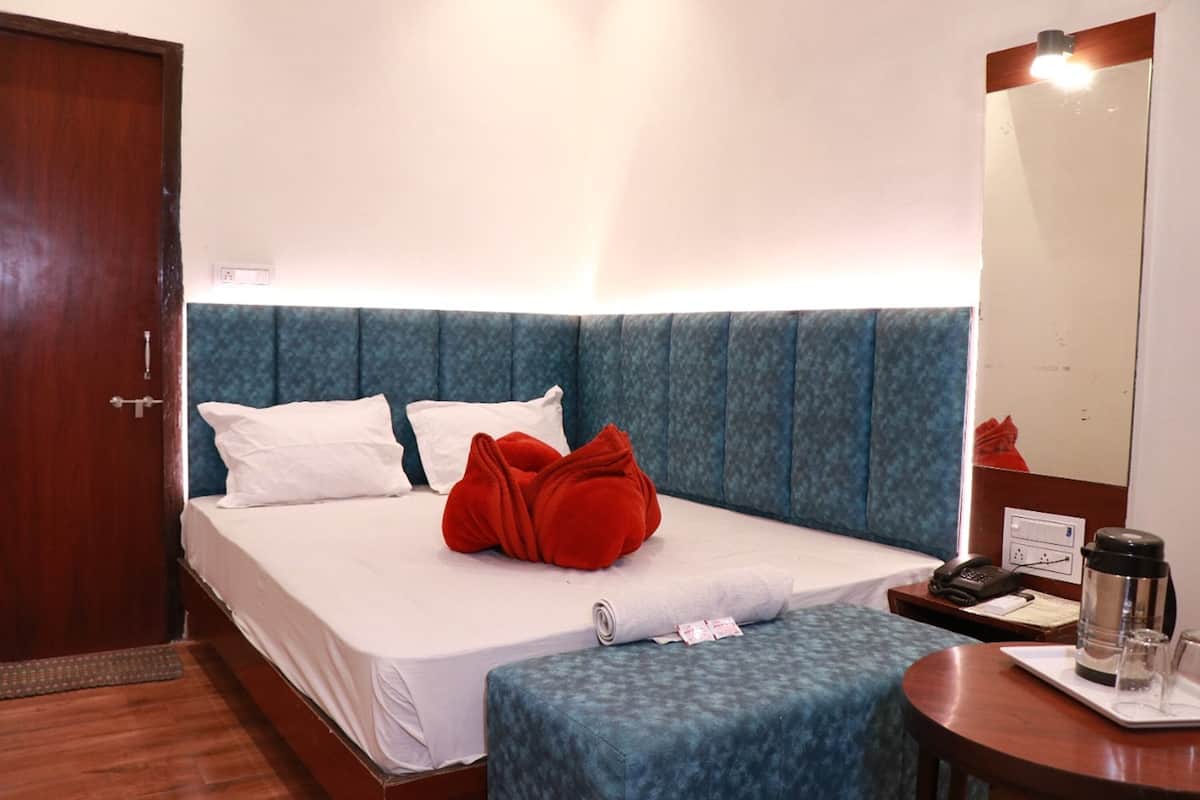 A hotel room with a bed, a bedside table with a phone and a coffee pot, a small table with glasses and a tray, and a mirror on the wall.