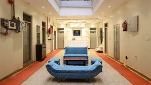 A hotel lobby with a central seating area, a high ceiling, and a visible fire extinguisher. - Hotel Amrit Near Old Delhi Railway Station (New Delhi)