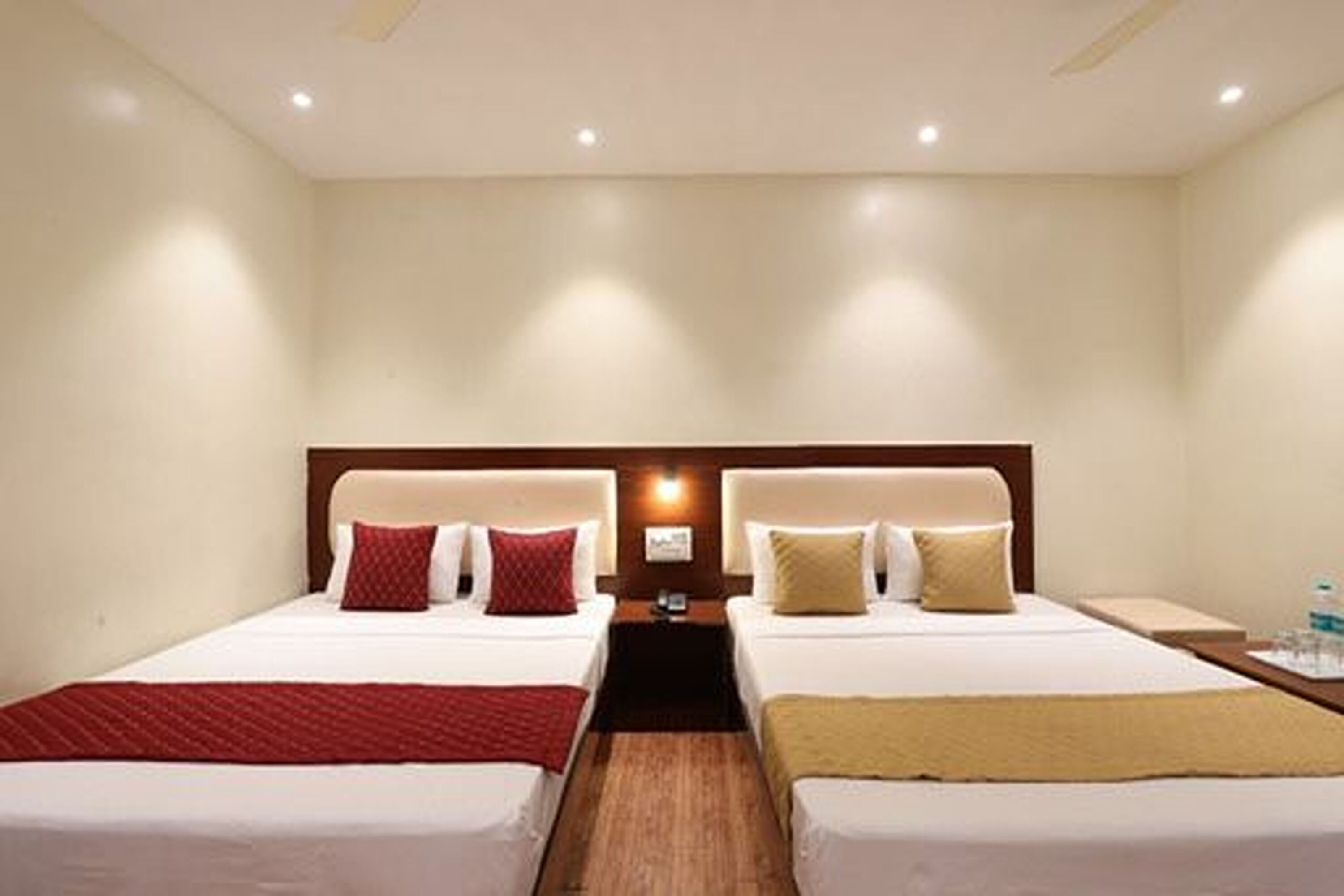 Habitación de hotel con dos camas, cada una con cabecera, mesita de noche y lámpara de pared.