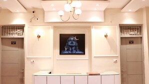 A reception area with a central counter, two doors, a chandelier, and a framed artwork on the wall. - Hotel Amrit Near Old Delhi Railway Station (New Delhi)