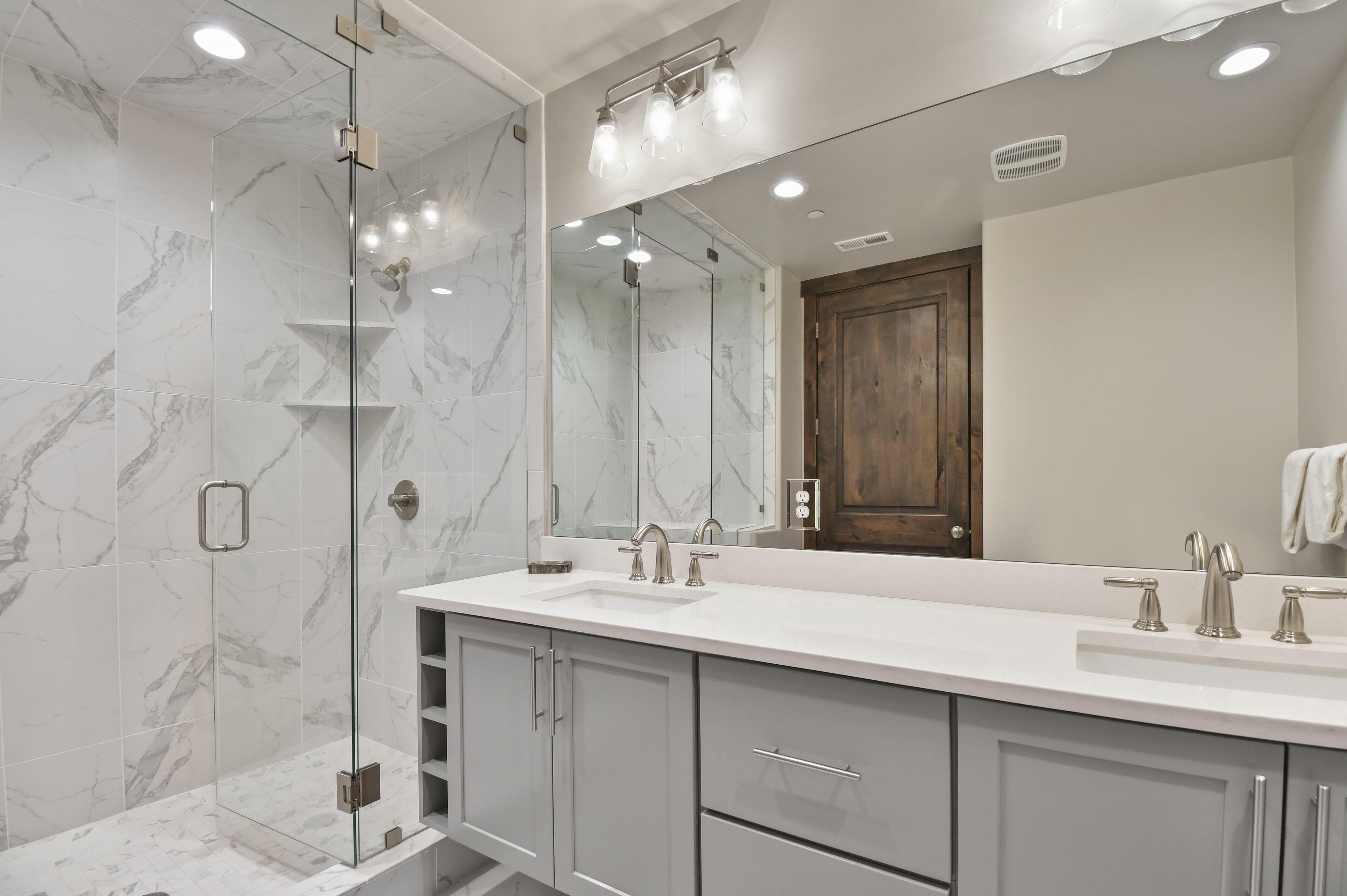 A modern bathroom with a glass-enclosed shower, a large mirror, and a white vanity with two sinks.