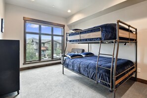 Habitación con literas, un ventanal grande, suelo cubierto de alfombra y televisor.