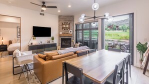 A modern living room with a sofa, dining table, and a TV mounted on the wall.