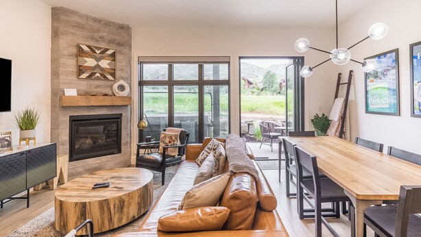 A modern living room with a fireplace, large windows, and a dining area.
