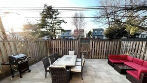 A patio with a grill, a dining table with chairs, and a red sofa.