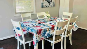A dining area with a round table, white chairs, and a floral tablecloth.