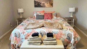 A bedroom with a bed, two nightstands, a bench with folded clothes, and a beach-themed painting on the wall.