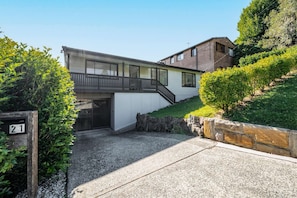 A modern two-story house with a balcony, a garage, and a stone retaining wall. - "Family Tides" – Short Stroll to the Beach (Copacabana)