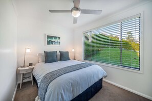 A bedroom with a bed, two bedside tables, a ceiling fan, a window with blinds, and a framed picture on the wall. - "Family Tides" – Short Stroll to the Beach (Copacabana)