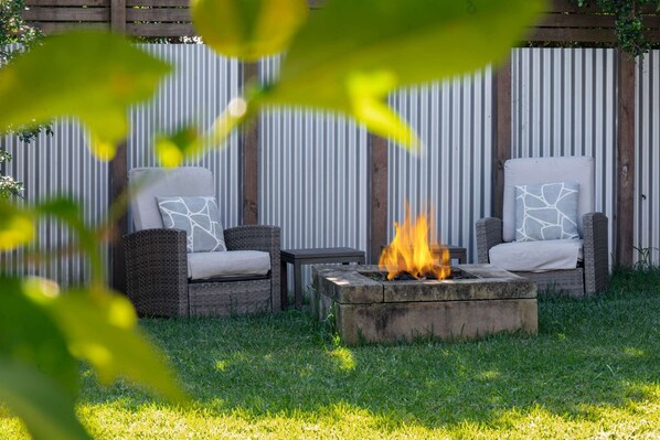 Two wicker chairs with cushions, a small table, and a fire pit with flames. - "Family Tides" – Short Stroll to the Beach (Copacabana)