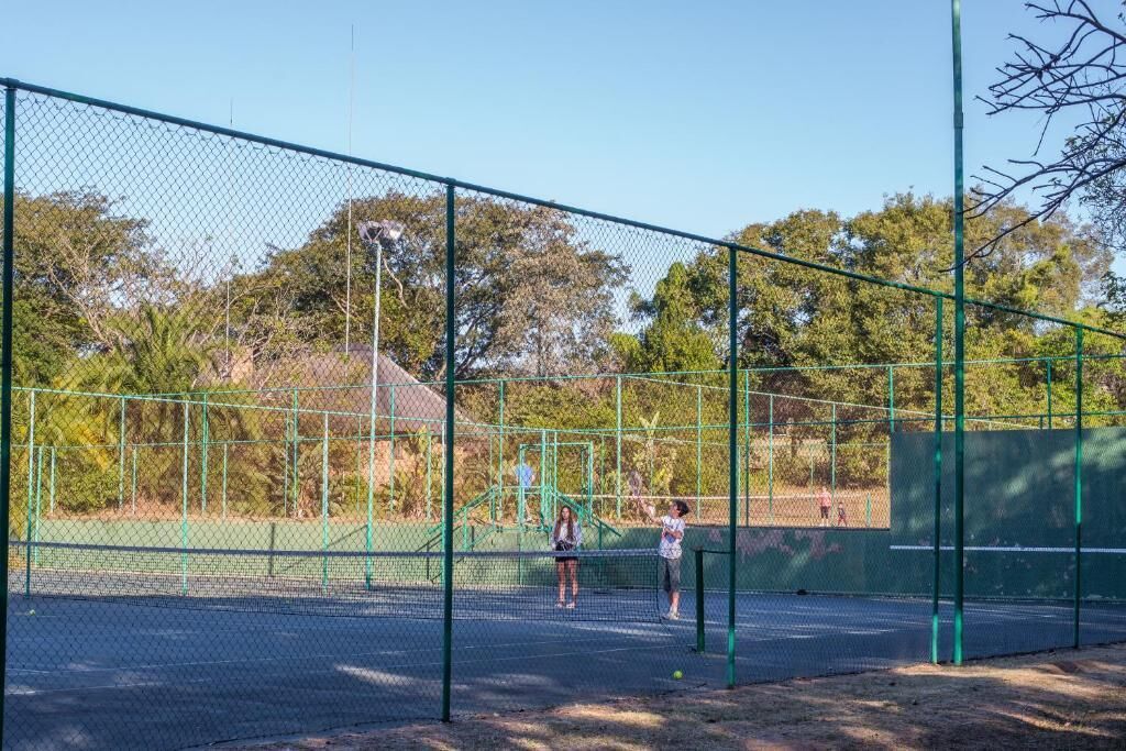 Ein Tennisplatz im Freien mit grünem Zaun und Netz, auf dem zwei Personen spielen.