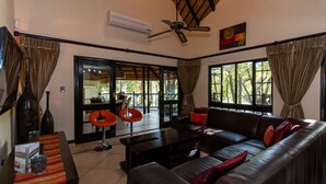 A living room with a sofa, a coffee table, and a TV. There is a ceiling fan and a window with curtains. - Kruger Park Lodge Unit No. 209 (Mbombela)