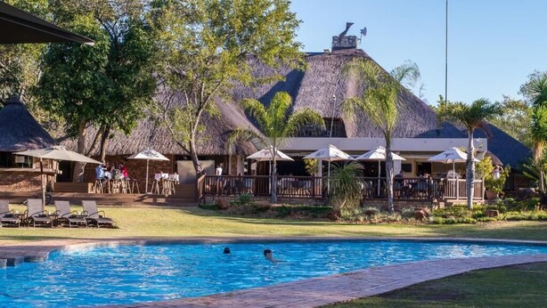 A swimming pool with lounge chairs and umbrellas, surrounded by buildings with thatched roofs and outdoor seating areas. - Kruger Park Lodge Unit No. 209 (Mbombela)