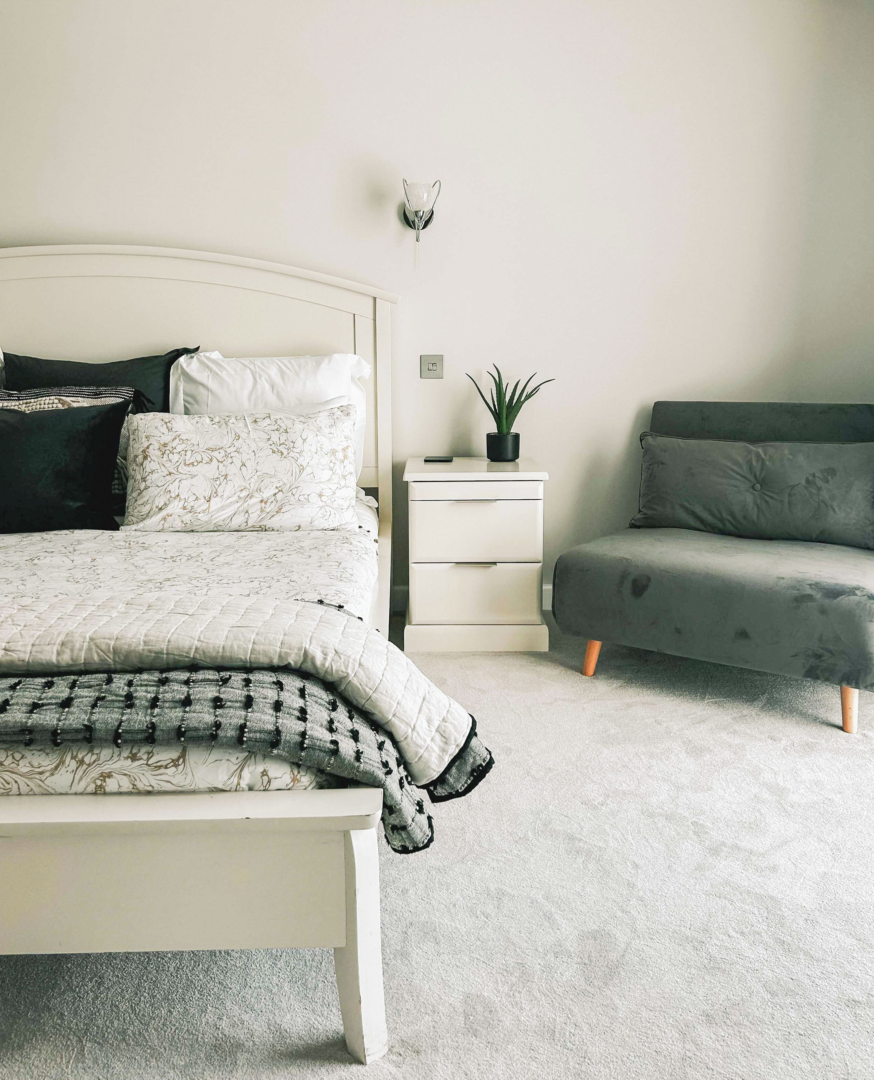 Une chambre à coucher avec un lit, une table de chevet, une commode et un canapé gris.