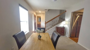 A dining area with a wooden table, black chairs, and a vase with flowers. There is a staircase with a wooden railing leading to another room. - Two-story, two-bedroom, blocks from Downtown New Braunfels, Comal River, and Texas Tubes (New Braunfels)