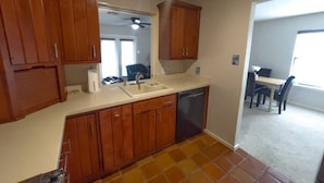 A kitchen with wooden cabinets, a sink, and a dishwasher. There is a dining area with a table and chairs visible in the background. - Two-story, two-bedroom, blocks from Downtown New Braunfels, Comal River, and Texas Tubes (New Braunfels)