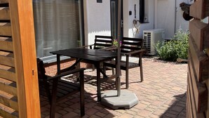 Un patio con una mesa y sillas bajo un gran paraguas, suelo de ladrillo y un edificio blanco al fondo.