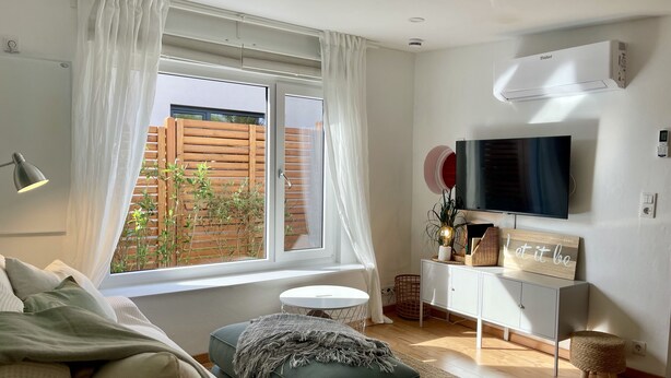 Una sala de estar moderna con un ventanal grande, un televisor de pantalla plana, un mueble blanco y una zona de estar acogedora.