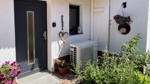 Una casa con una puerta oscura, una ventana pequeña, una decoración con forma de corazón y una maceta colgante.