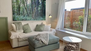 Un salón acogedor con sofá, reposapiés y un cuadro de gran tamaño con motivos forestales.