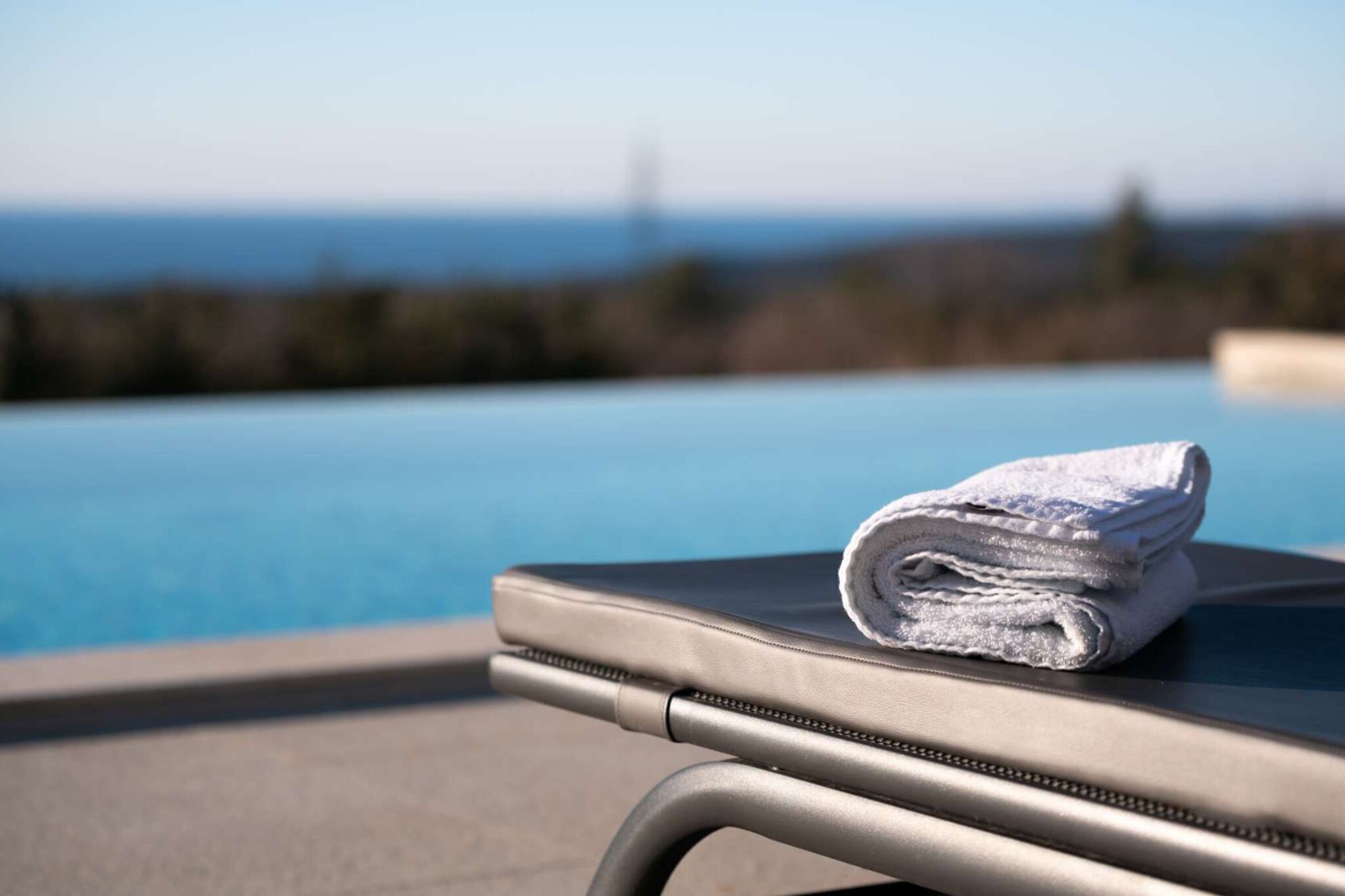 A poolside lounge chair with a folded towel and a clear view of the ocean in the background.