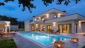A modern two-story house with a swimming pool, outdoor seating, and well-lit windows. - Stylish Villa with Pool (Labin)