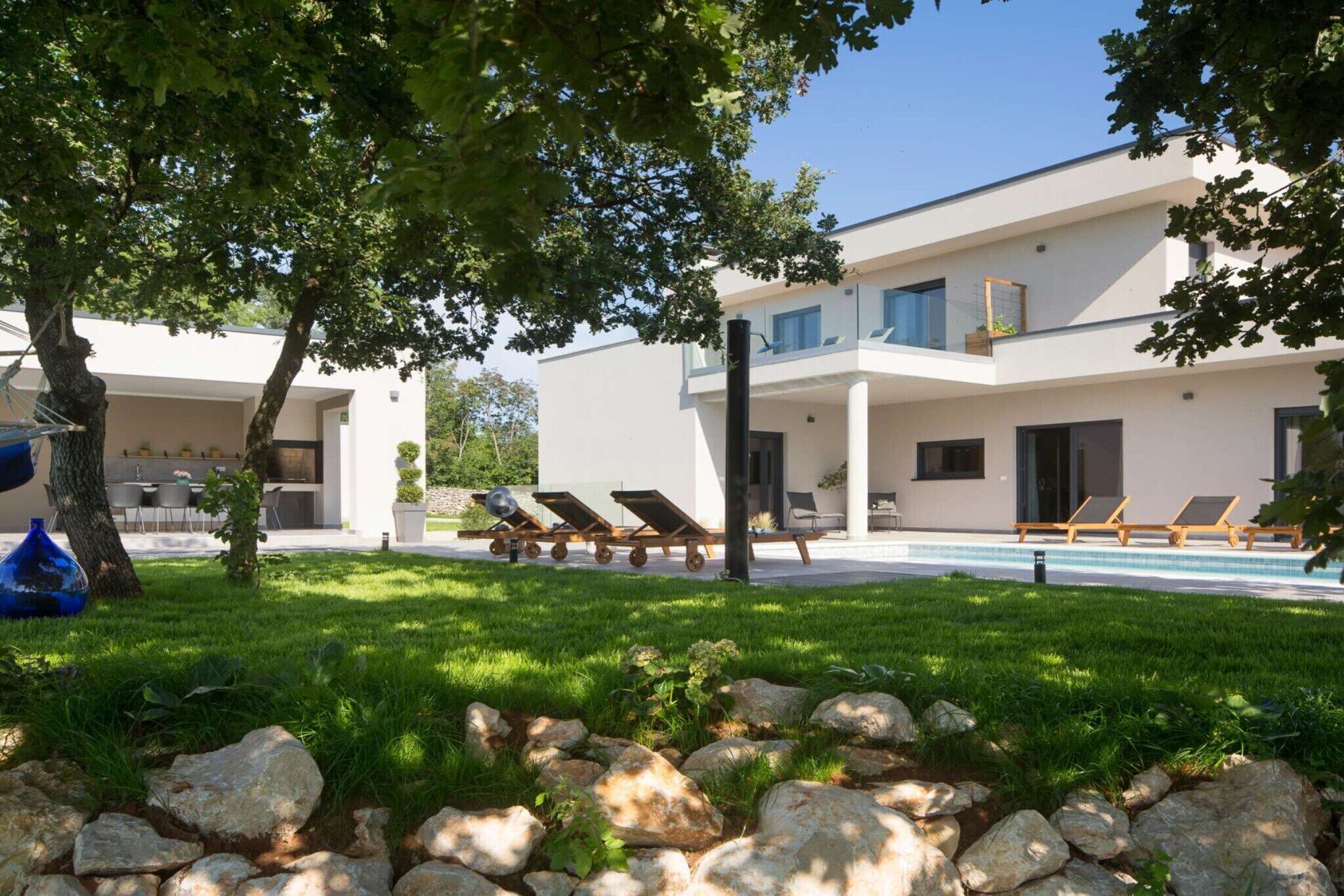 A modern two-story building with a swimming pool, lounge chairs, and a well-maintained lawn.