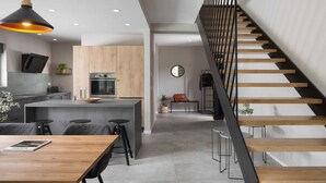 A modern kitchen with a central island, a dining area with a wooden table, and a staircase with a black railing. - Stylish Villa with Pool (Labin)