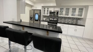 Une cuisine moderne avec des armoires blanches, un comptoir noir et des appareils en acier inoxydable. On trouve deux tabourets de bar noirs devant le comptoir.