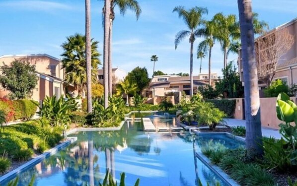 Relax by the tranquil pool surrounded by lush greenery and palm trees.