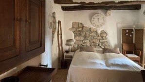 A rustic bedroom with a stone wall, wooden bed, and a large wooden wardrobe. - Pleasant holiday home in Vrbnik near Secret Beach (Vrbnik)