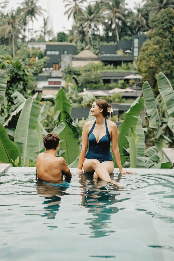 A couple in a swimming pool with lush greenery and a modern building in the background.